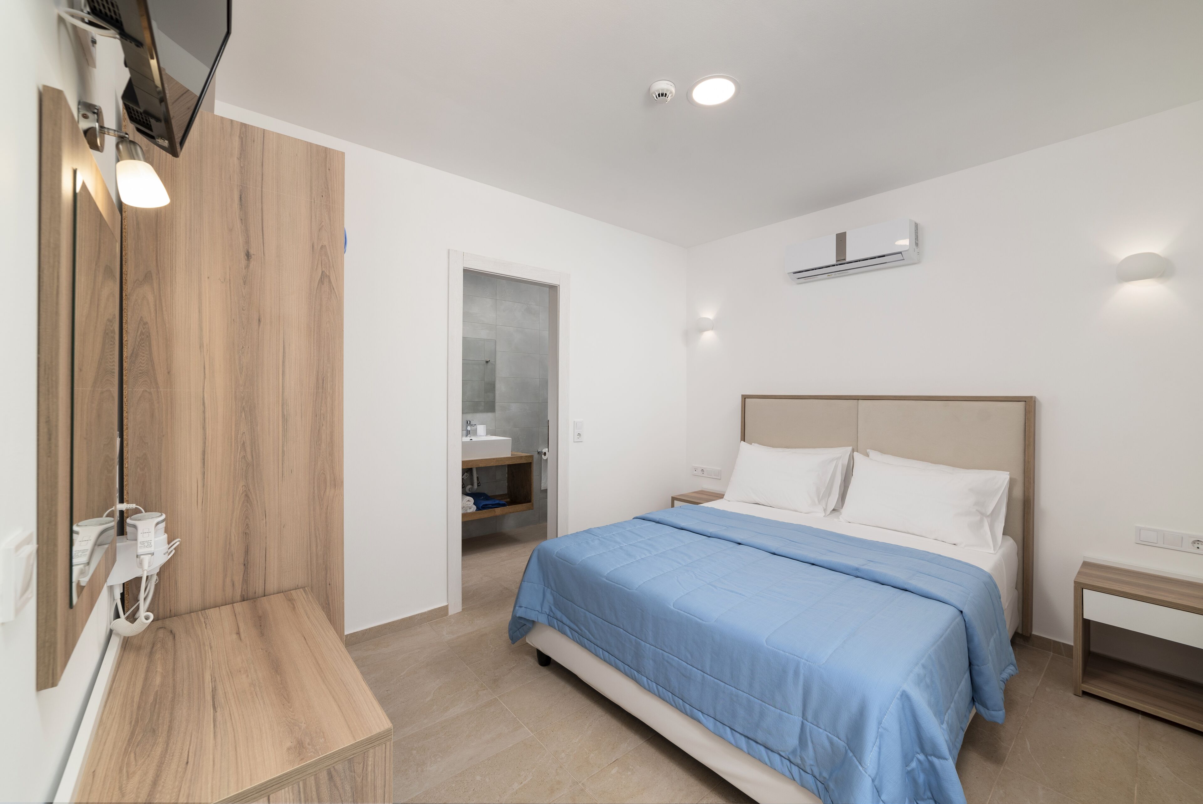 A modern bedroom with a large bed, bedside tables, a wooden bench, a mirror, and an air conditioning unit.