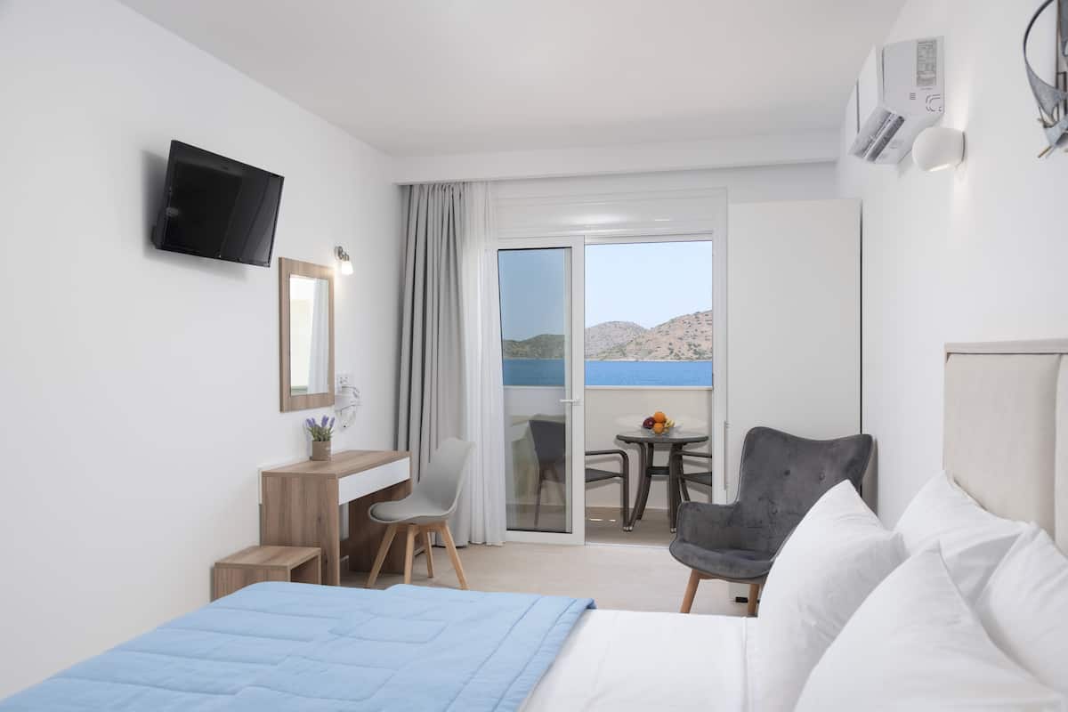 Habitación de hotel con cama, escritorio, silla, televisor y balcón con vistas a las montañas.