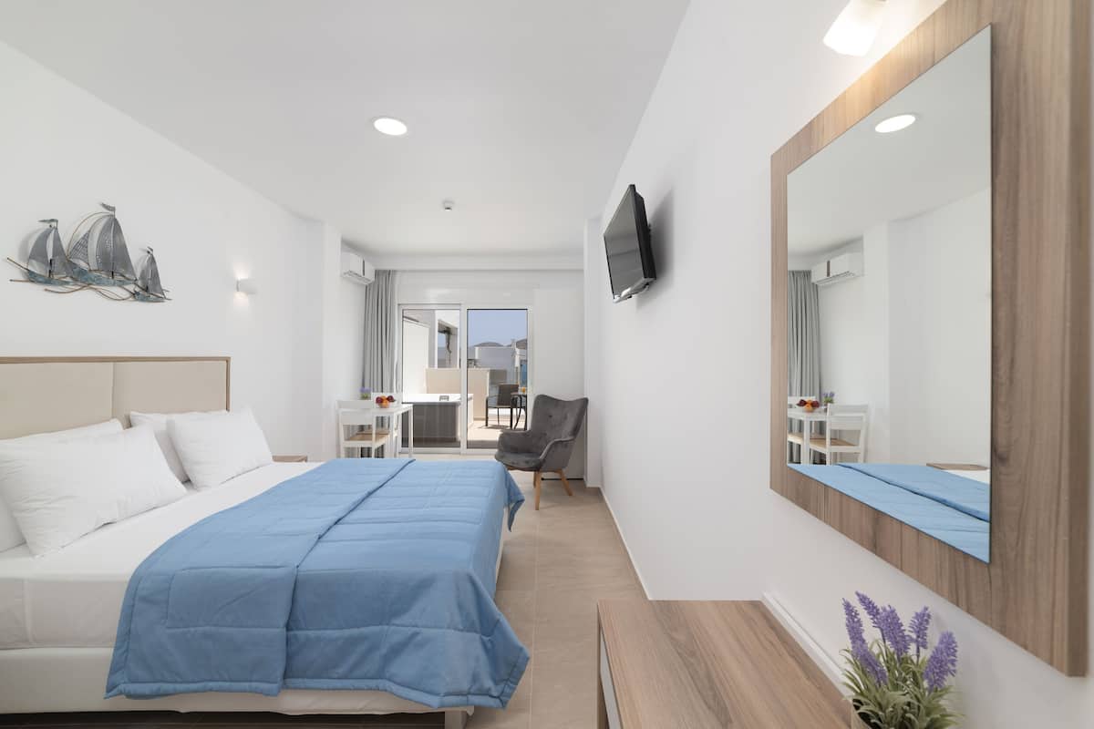 Una habitación de hotel moderna con cama, escritorio, silla, televisor y un espejo grande.