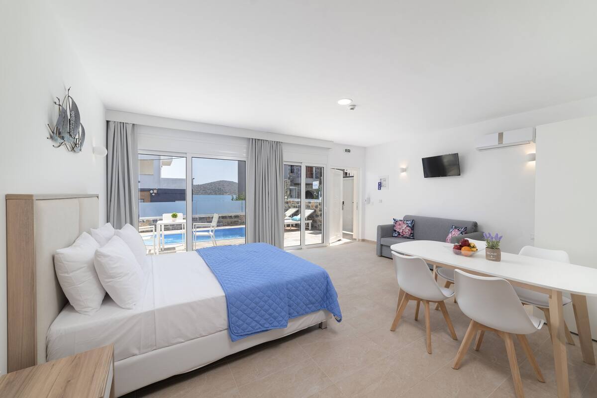 Una habitación de hotel moderna con una cama, una mesa de comedor con sillas, un televisor y vista al mar.