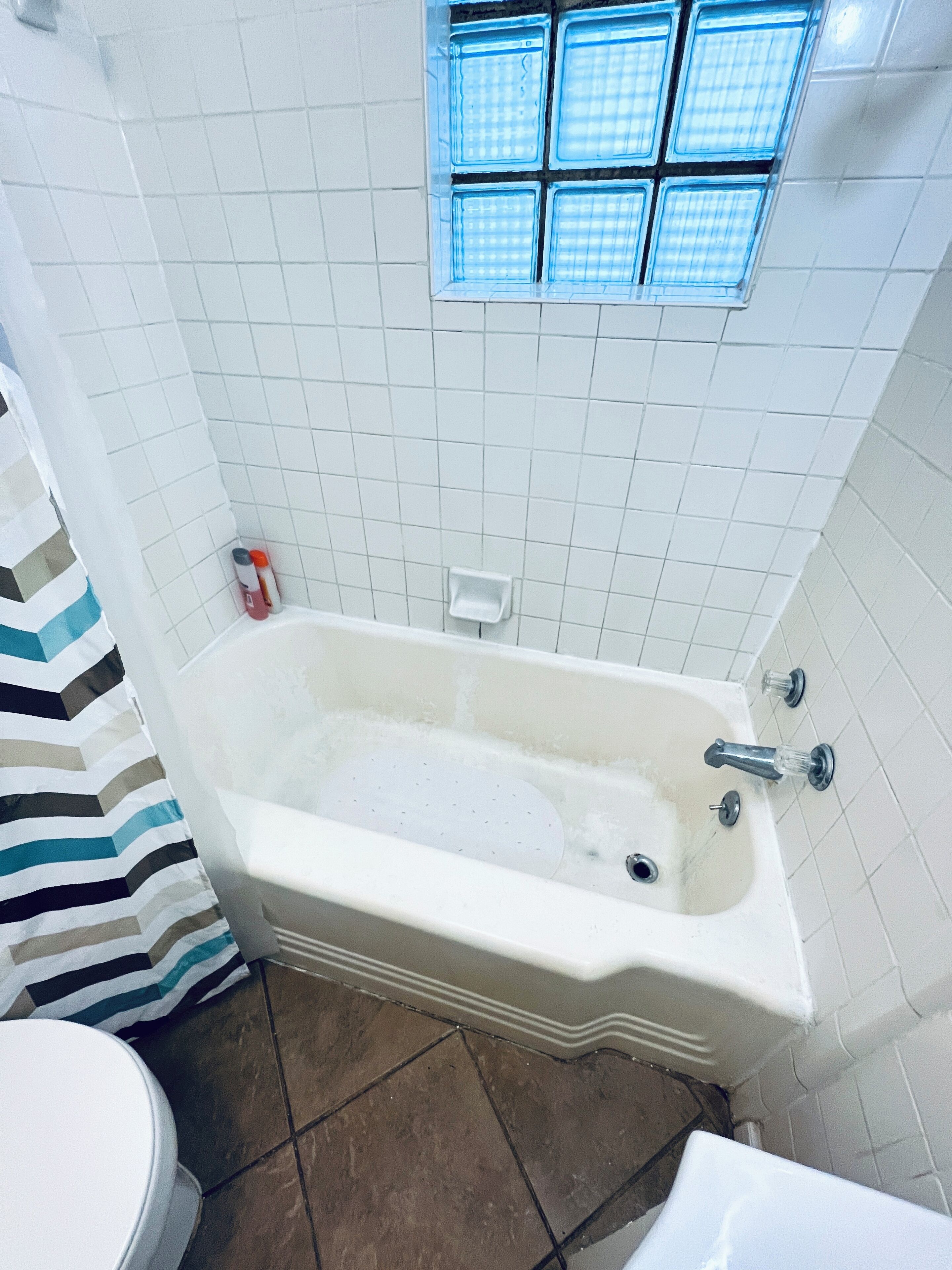 A bathroom with a bathtub, white tiled walls, a window, and a striped shower curtain.