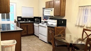 A compact kitchen with wooden cabinets, a stove, microwave, and a glass dining table with chairs. - Harlan, KY Modern Private Guesthouse 302 Historic Downtown (Vela's Villas) (Harlan)