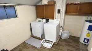 A compact laundry room with two washing machines, a drying rack, a small table, and a radiator. - Harlan, KY Modern Private Guesthouse 302 Historic Downtown (Vela's Villas) (Harlan)