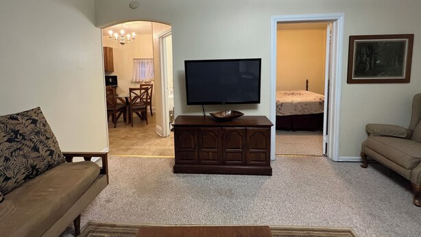 A living room with a flat-screen TV on a wooden cabinet, a sofa, a chair, and a dining area in the background. - Harlan, KY Modern Private Guesthouse 302 Historic Downtown (Vela's Villas) (Harlan)