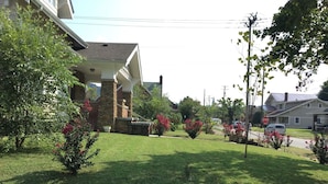 Un quartier résidentiel où se trouve une maison avec une façade en pierre et en briques, un porche abrité et une pelouse bien entretenue agrémentée d’arbustes en fleurs.