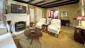 Un salon avec une cheminée, deux fauteuils, une table basse et un téléviseur.