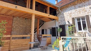 A two-story stone building with a wooden balcony and a staircase leading to the upper floor. - SPACIOUS APARTMENT**** BALCONY, TERRACE, GARDEN, PARKING + CHARGING STATION, AIR CONDITIONING (MONTAIGU)