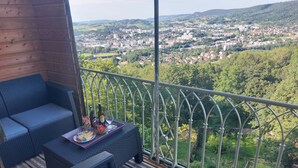A balcony with a view of a town and hills. There is a sofa and a table with a tray of food and drinks. - SPACIOUS APARTMENT**** BALCONY, TERRACE, GARDEN, PARKING + CHARGING STATION, AIR CONDITIONING (MONTAIGU)