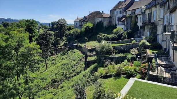 A hillside residential area with terraced houses, lush greenery, and a church spire. - SPACIOUS APARTMENT**** BALCONY, TERRACE, GARDEN, PARKING + CHARGING STATION, AIR CONDITIONING (MONTAIGU)