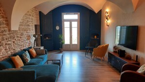 A living room with a stone wall, a blue door, a sofa, a TV, and a fireplace. - SPACIOUS APARTMENT**** BALCONY, TERRACE, GARDEN, PARKING + CHARGING STATION, AIR CONDITIONING (MONTAIGU)