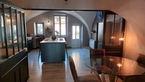 A spacious kitchen with an island, a dining area with a glass table, and a cozy seating arrangement. - SPACIOUS APARTMENT**** BALCONY, TERRACE, GARDEN, PARKING + CHARGING STATION, AIR CONDITIONING (MONTAIGU)