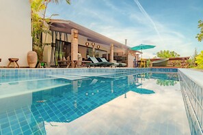 Piscina con sillas de descanso y una zona de estar cubierta.