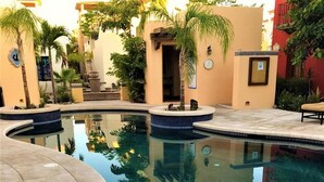 A swimming pool with a tiled edge, surrounded by palm trees and buildings with a Mediterranean architectural style.