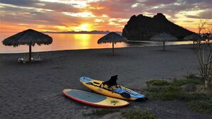 A beach with kayaks and thatched umbrellas.