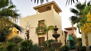 A courtyard with a fountain, palm trees, and a building with a balcony.