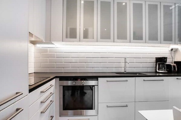Une cuisine moderne avec des meubles blancs, un four en acier inoxydable et un plan de travail noir.