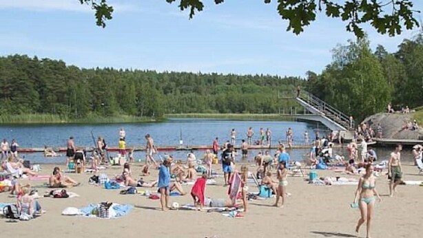 Een druk strand met mensen die zonnebaden en zwemmen.