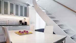 Een moderne keuken met witte kastjes, een eettafel met stoelen en een trap met een opvallend ontwerp.