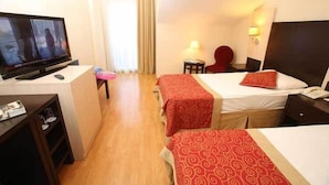 A hotel room with a TV, two beds with red and white bedding, a desk with a lamp, and a chair.