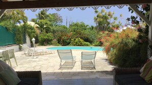 Eine Terrassenanlage mit zwei Korbsesseln, einem Tisch mit einer Vase und einem Pool im Hintergrund.