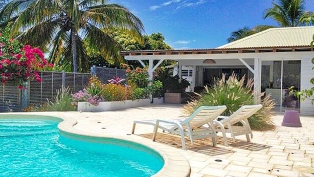 Ein Schwimmbecken mit gewölbter Kante, umgeben von Liegestühlen und einer überdachten Terrasse.