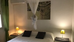 Ein ordentlich gemachtes Bett mit weißer Bettdecke, zwei schwarzen Kissen und einem Baldachin. Zwei Nachttische mit Lampen befinden sich auf jeder Seite des Bettes. Über dem Bett hängt ein Gemälde.