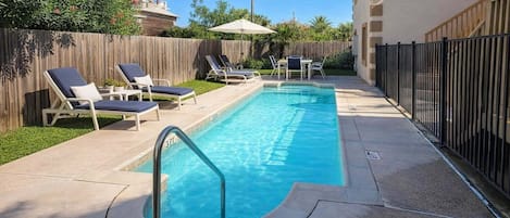 Una piscina rectangular con un indicador de profundidad de 3 pies, rodeada de sillas de descanso y una valla de madera.