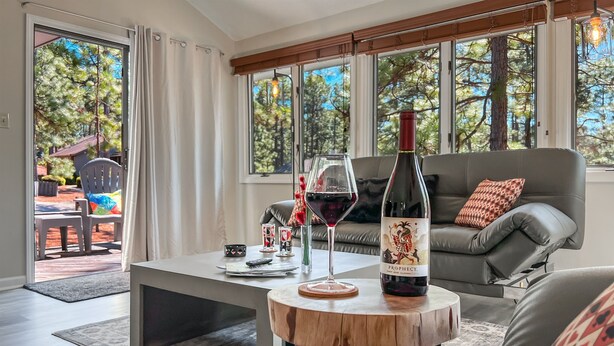Una sala moderna con una mesa de centro, una botella de vino y copas. Hay un sofá y una vista al exterior a través de amplios ventanales.
