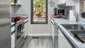 Una cocina moderna con electrodomésticos de acero inoxidable, una ventana con vistas a la vegetación y una encimera con cafetera y pasteles.