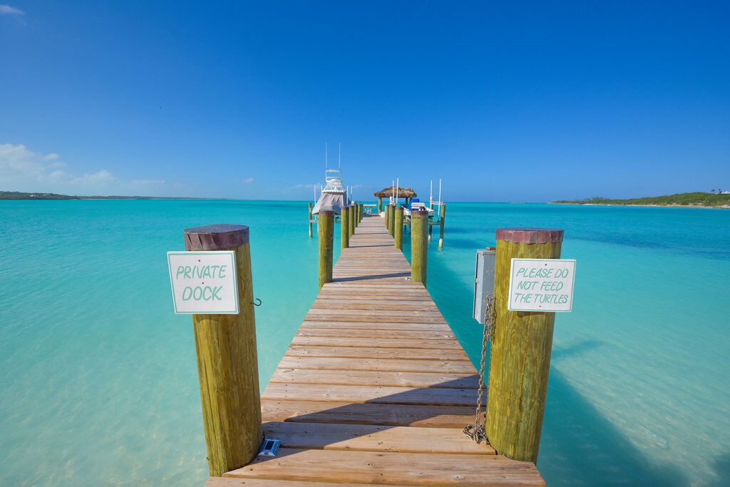 A wooden pier leading to a private dock with a sign warning not to feed turtles.