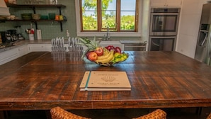 Une table de salle à manger en bois, avec un panier de fruits et un livre d’or au centre.