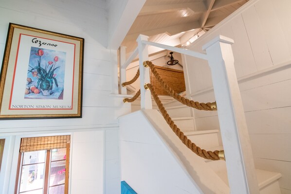 Una escalera con barandilla de cuerda y una obra de arte enmarcada arriba.