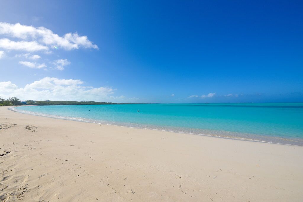 Une vaste plage de sable fin, bordée d’une eau turquoise et limpide, et surplombée d’un ciel dégagé.