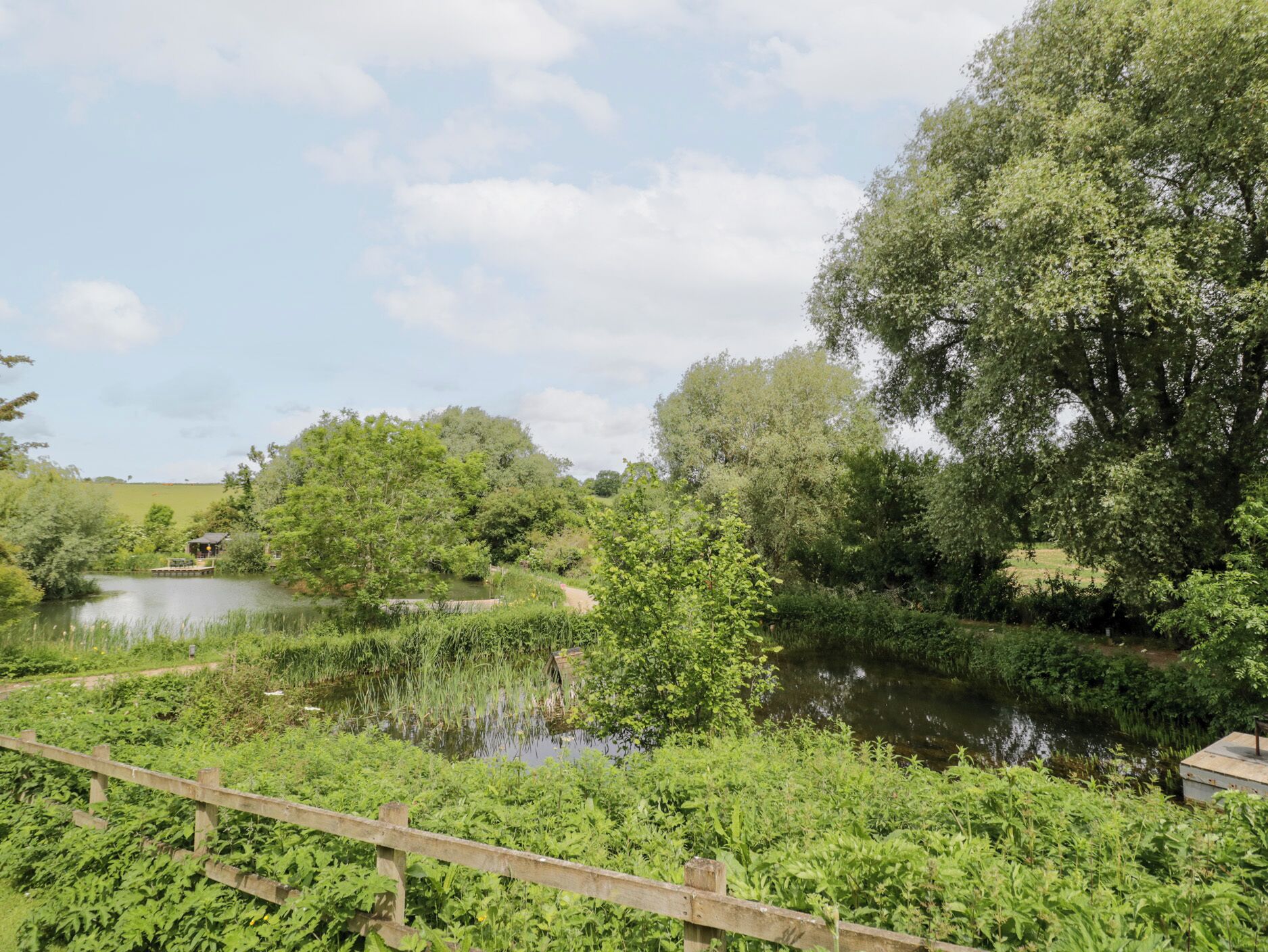 A serene riverside setting with a wooden bridge, lush greenery, and a small building by the water.