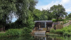 Uma cabana à beira do lago com um alpendre, rodeada por vegetação densa e um lago tranquilo.