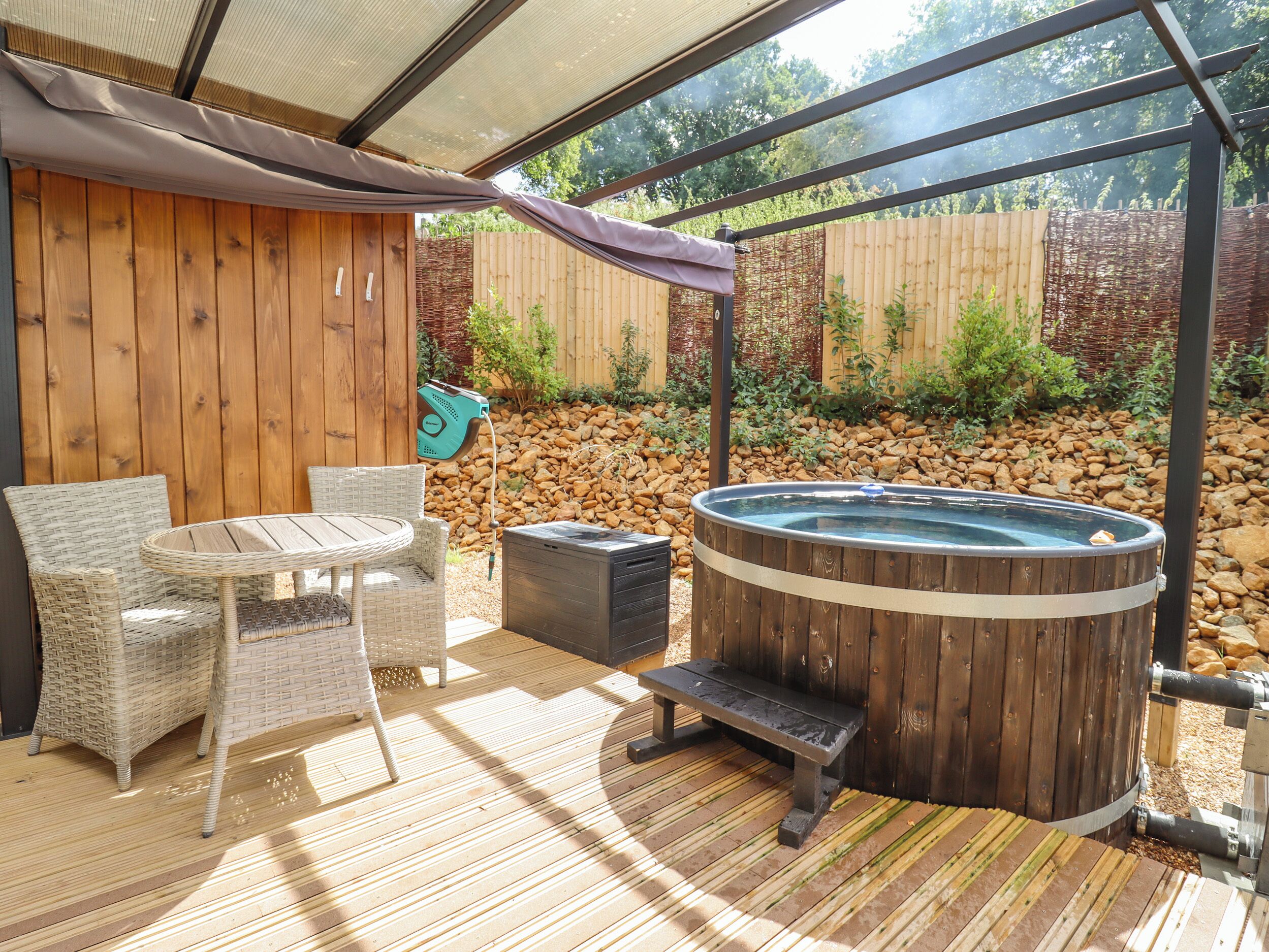 A wooden deck with a hot tub, wicker chairs, and a table.