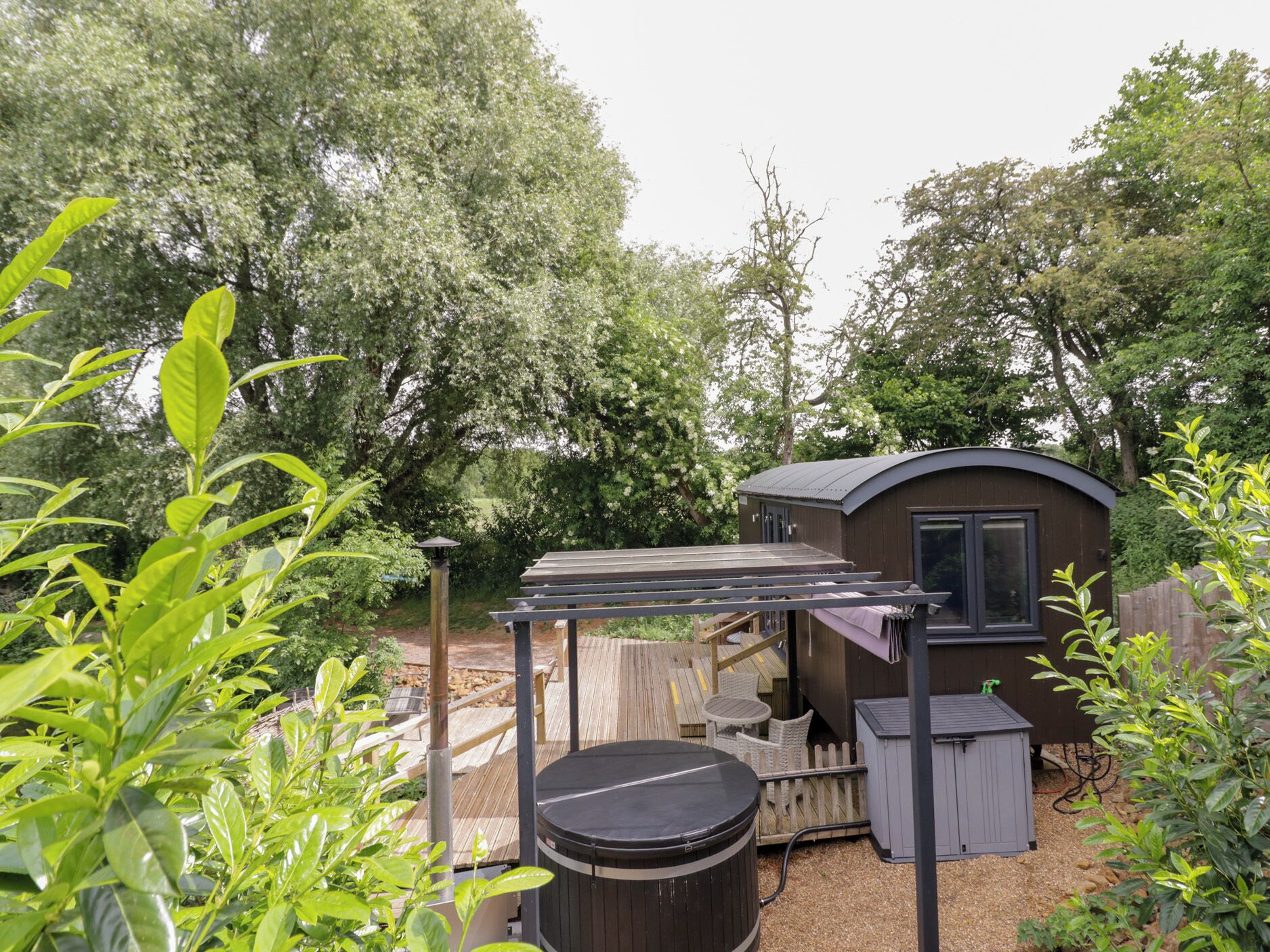 A small wooden cabin with a deck, surrounded by lush greenery and trees.