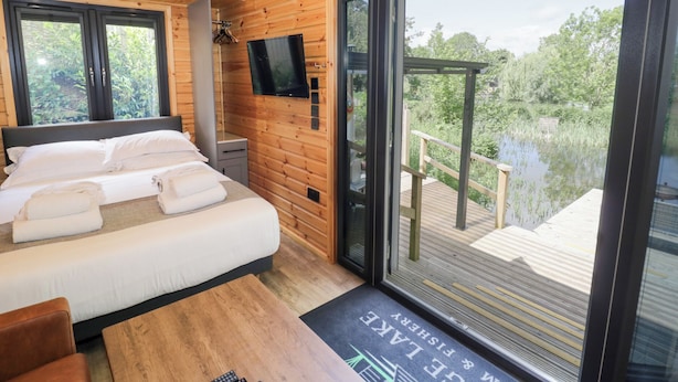 Quarto com cama grande, televisão na parede e varanda com vista para um lago.