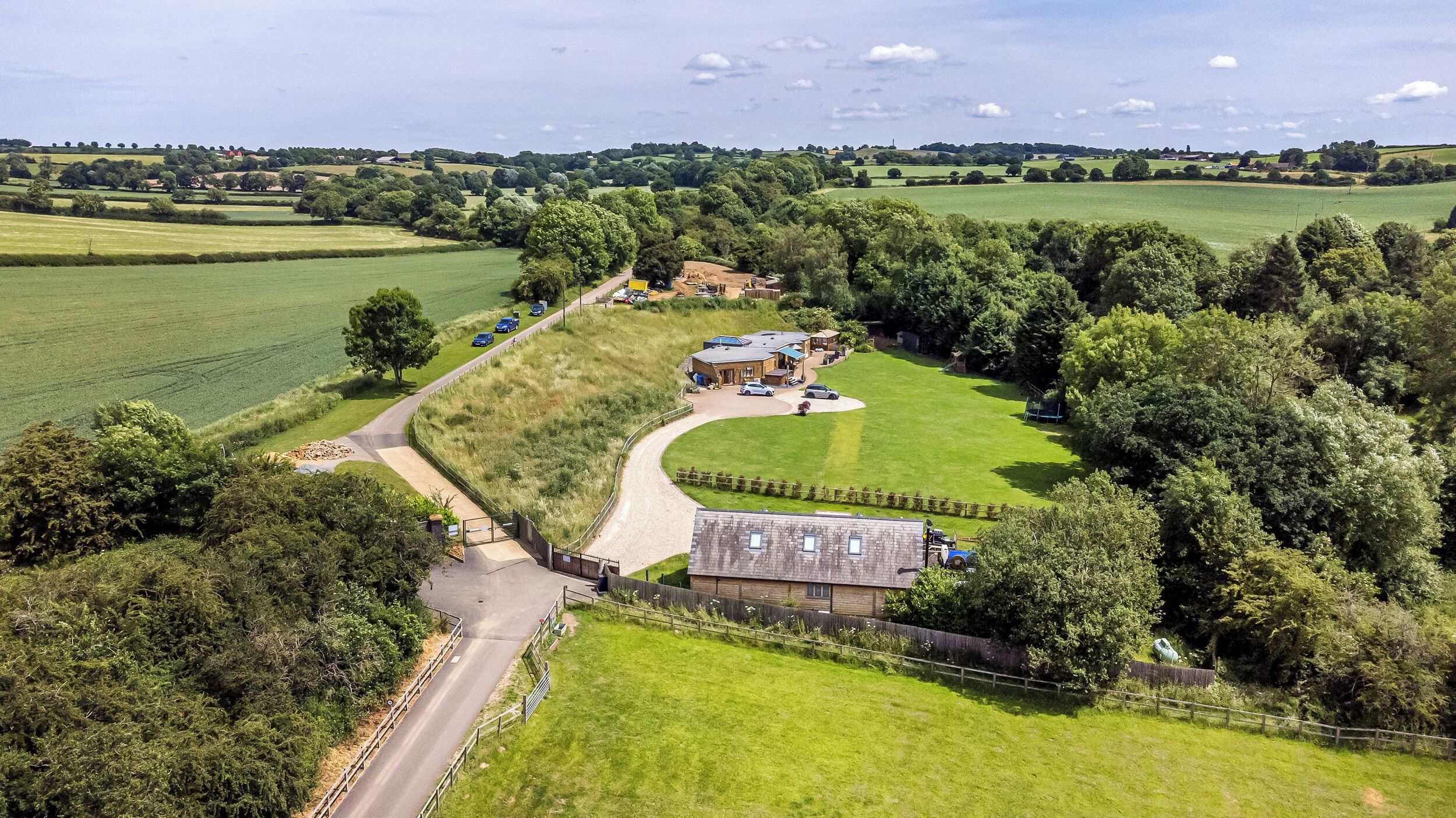 An aerial view of a rural property with a large green field, a farmhouse, and a winding road.