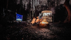 Un autobús amb una foguera i dues cadires en un bosc de nit.