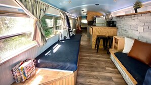 Interior d'una caravana compacta amb cuineta, zona de seients i finestra amb cortines.