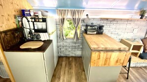 Cuina compacta amb taulell de fusta, forn encastrat i una petita finestra amb cortines.