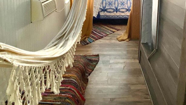 Un passadís estret amb una hamaca, un llit amb roba de llit estampada i una catifa rayada.