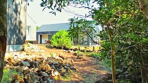 A modern house with a metal roof, surrounded by a garden with various plants and trees. - Casas do Morgadio - azorean wine & lodge (Praia da Vitoria)