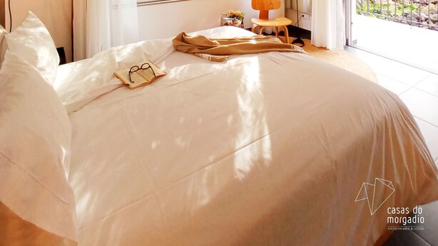 A bedroom with a large bed, a window with curtains, a hanging lamp, and a view of greenery outside. - Casas do Morgadio - azorean wine & lodge (Praia da Vitoria)