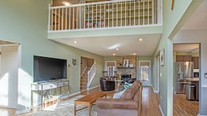 A spacious living area with a high ceiling, a staircase to an upper level, a fireplace, and a kitchen with modern appliances. - Private Hot Tub and Resort Amenities Included! (Massanutten)