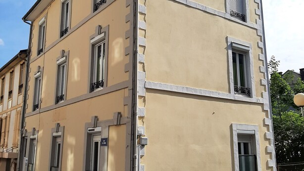 Un edificio a più piani con facciata beige, diverse finestre con persiane e un'entrata visibile.