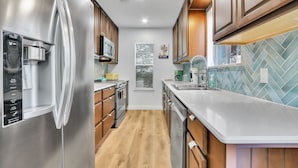 A modern kitchen with stainless steel appliances, wooden cabinets, and a herringbone tile backsplash. - Groovy Getaway | Lake Access, Pool, Tennis, 72-Hr Boat Parking (Canyon Lake)