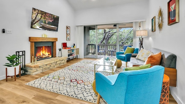 A spacious living room with a fireplace, blue sofas, a coffee table, and a large window overlooking a deck. - Groovy Getaway | Lake Access, Pool, Tennis, 72-Hr Boat Parking (Canyon Lake)
