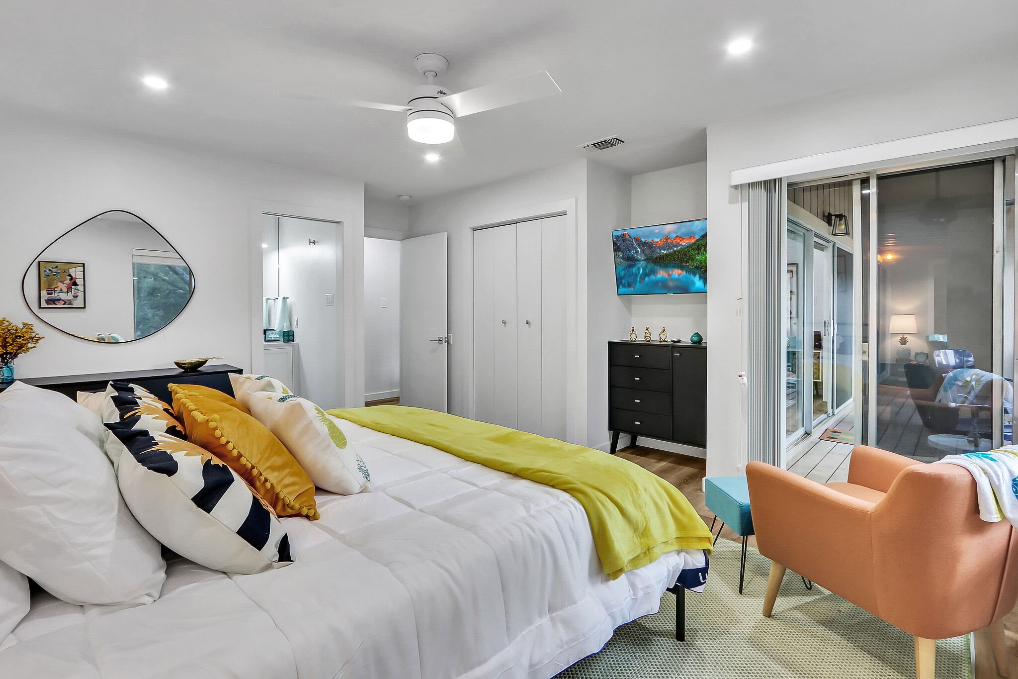 A modern bedroom with a bed, a desk, a chair, and a sliding glass door leading to a balcony.